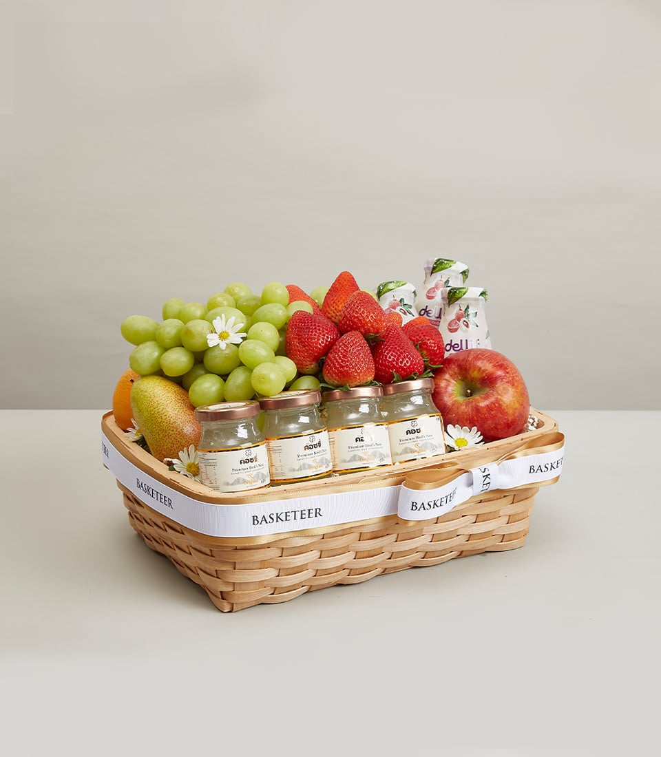 Woven fruit basket with fresh grapes, strawberries, pear, apple, wellness jars, and white daisies