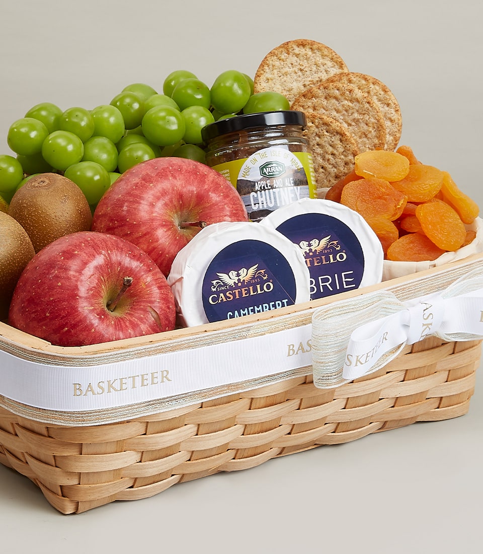 Woven gift basket with fresh fruits, artisan cheeses, crackers, and gourmet chutney tied with gold-striped ribbon