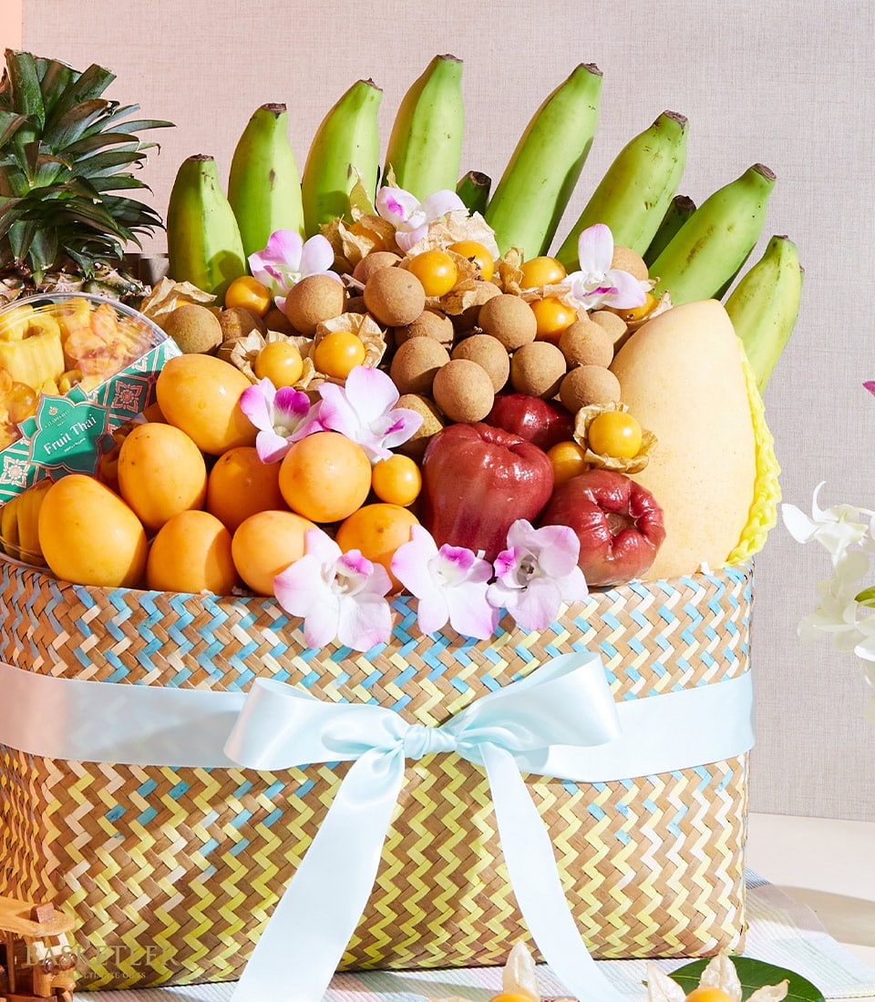 Premium woven fruit basket with Thai tropical fruits, longans, mangoes, rose apples, and fresh orchids, tied with blue satin