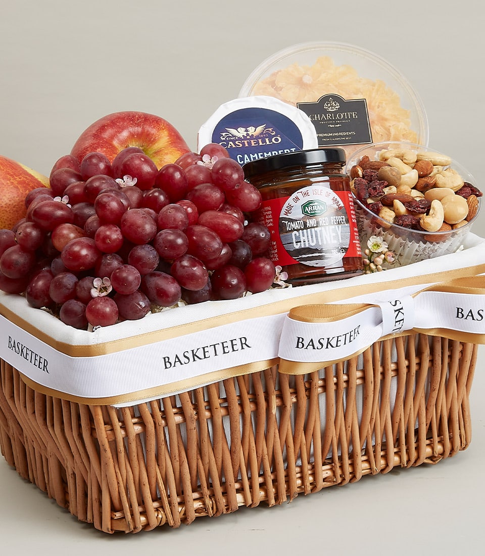 Gourmet fruit and cheese gift basket with grapes, pear, apple, Camembert, nuts, and chutney in wicker