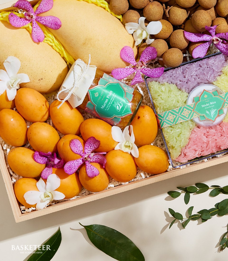 Luxury Thai tropical fruit gift box with fresh mangoes, Marian plums, orchids, and artisan sticky rice trio in wooden