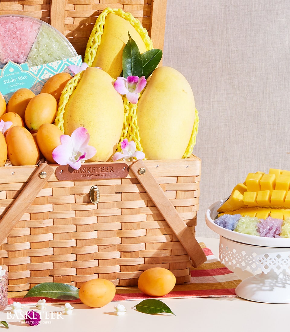 Woven picnic basket filled with ripe Thai mangoes, orchid blossoms, and colorful sticky rice portions