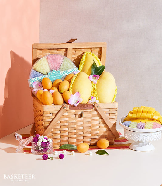 Woven picnic basket filled with Thai mangoes, tropical fruits, sticky rice dessert, and orchid blossoms