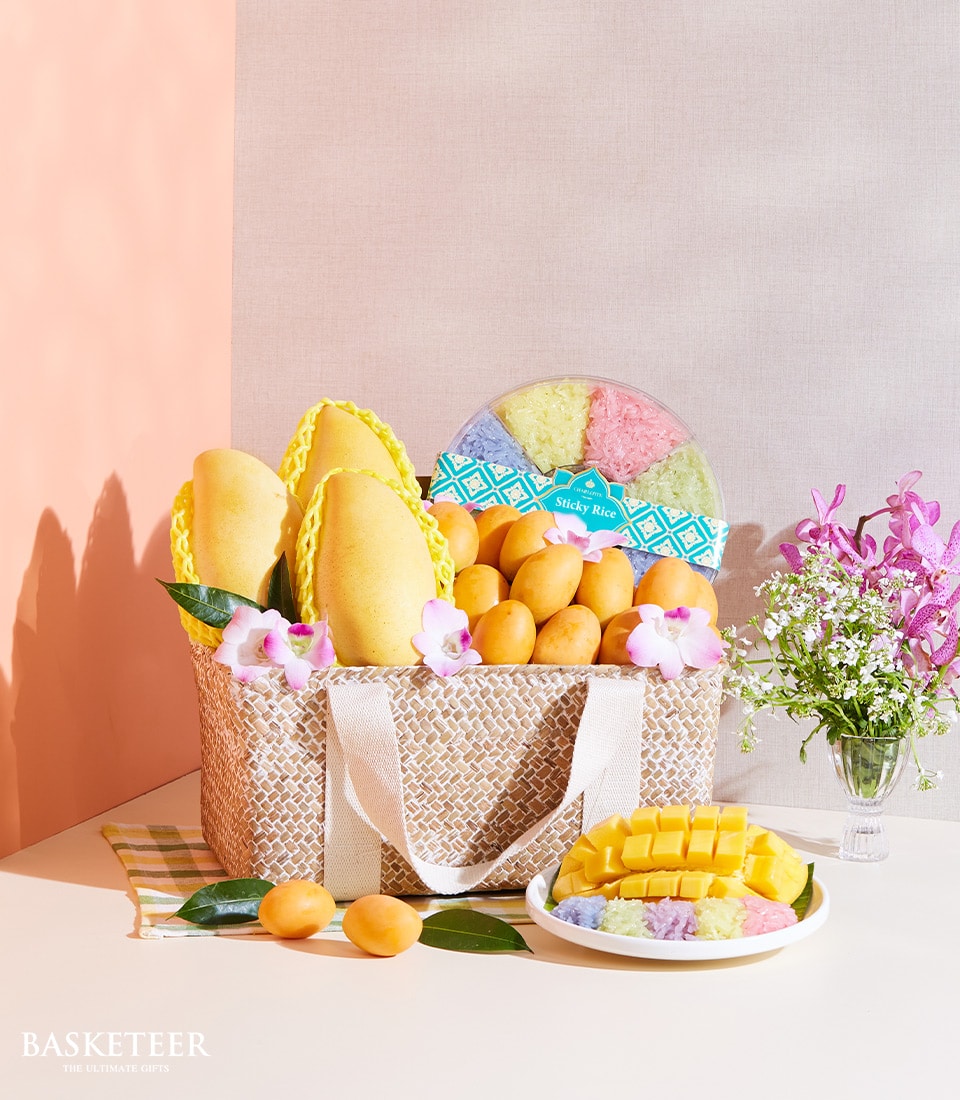 Woven gift basket with golden mangoes, plum fruits, colorful sticky rice, and pink orchids
