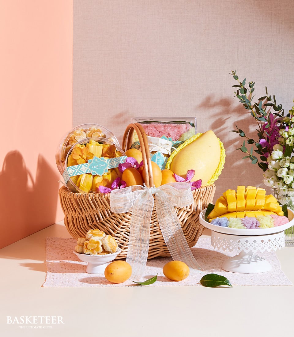 Woven wicker gift basket with Thai tropical fruits, mango, sticky rice, jackfruit, and layered sweets with white ribbon