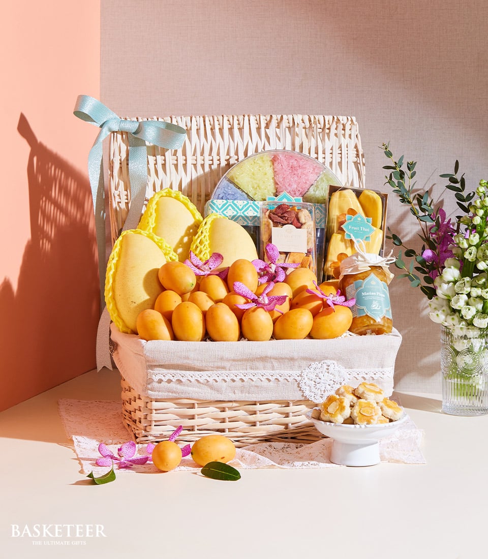 Wicker gift basket with Thai mangoes, tropical fruits, purple orchids, dried mango, nuts, and jam preserve with light blue