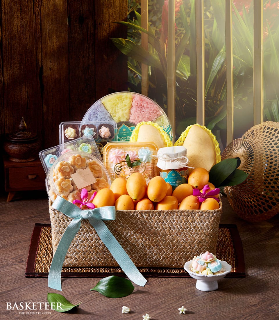 Woven straw gift basket with Thai fruits, mango, Marian plum jam, and assorted pastries tied with light blue ribbon