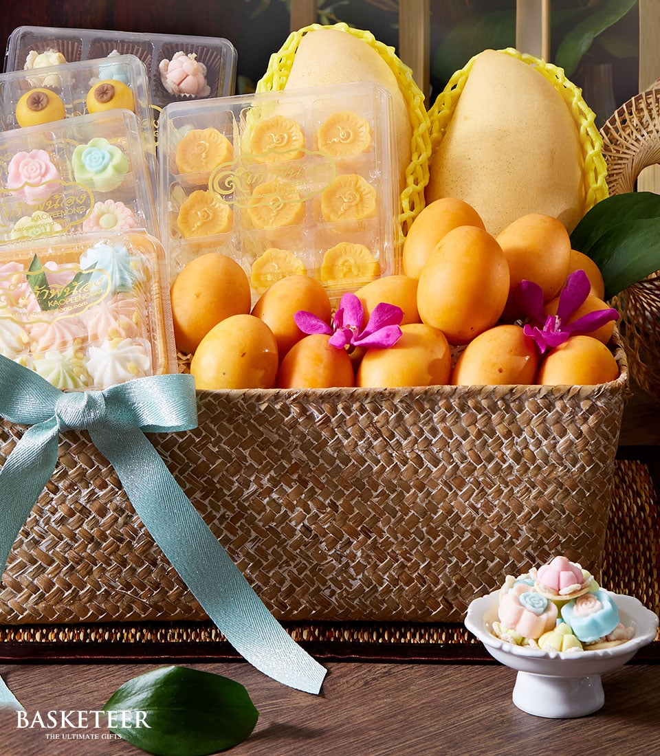 Yellow mangoes, apricots, and Thai desserts in woven basket with orchids for Songkran
