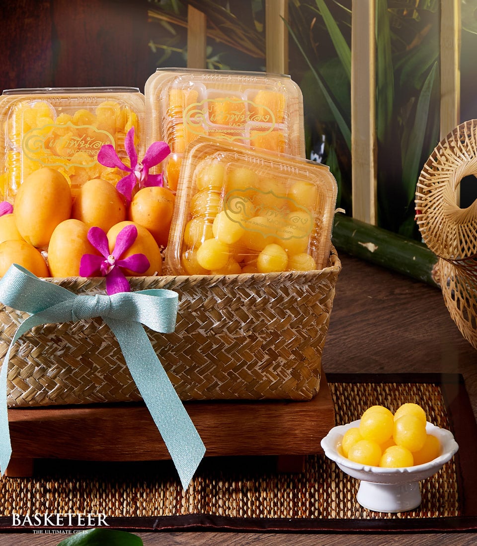 Woven gift basket of Thai desserts and Marian plums with purple orchids and blue ribbon, perfect for Thai New Year