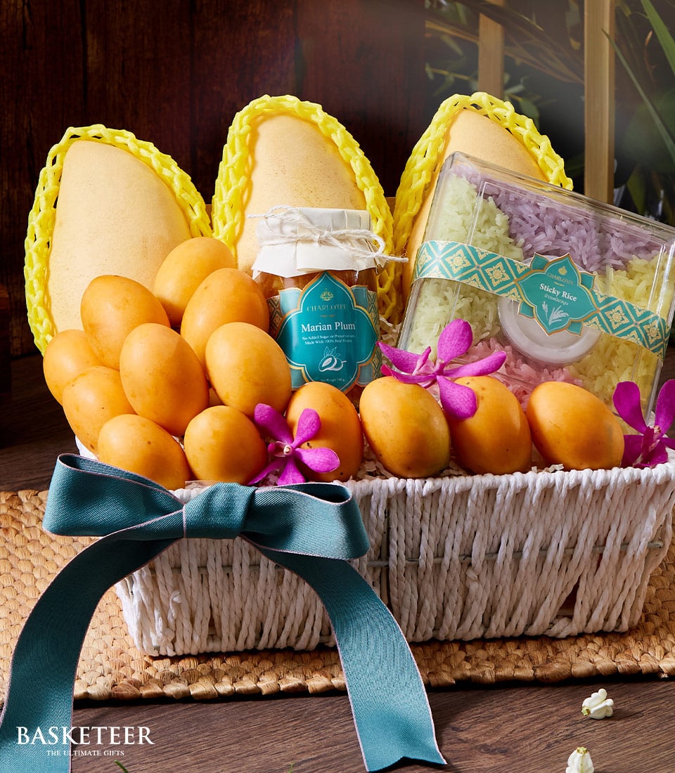 Woven white gift basket with fresh Thai mangoes, Marian plum jam, colorful sticky rice, and purple orchids tied with teal