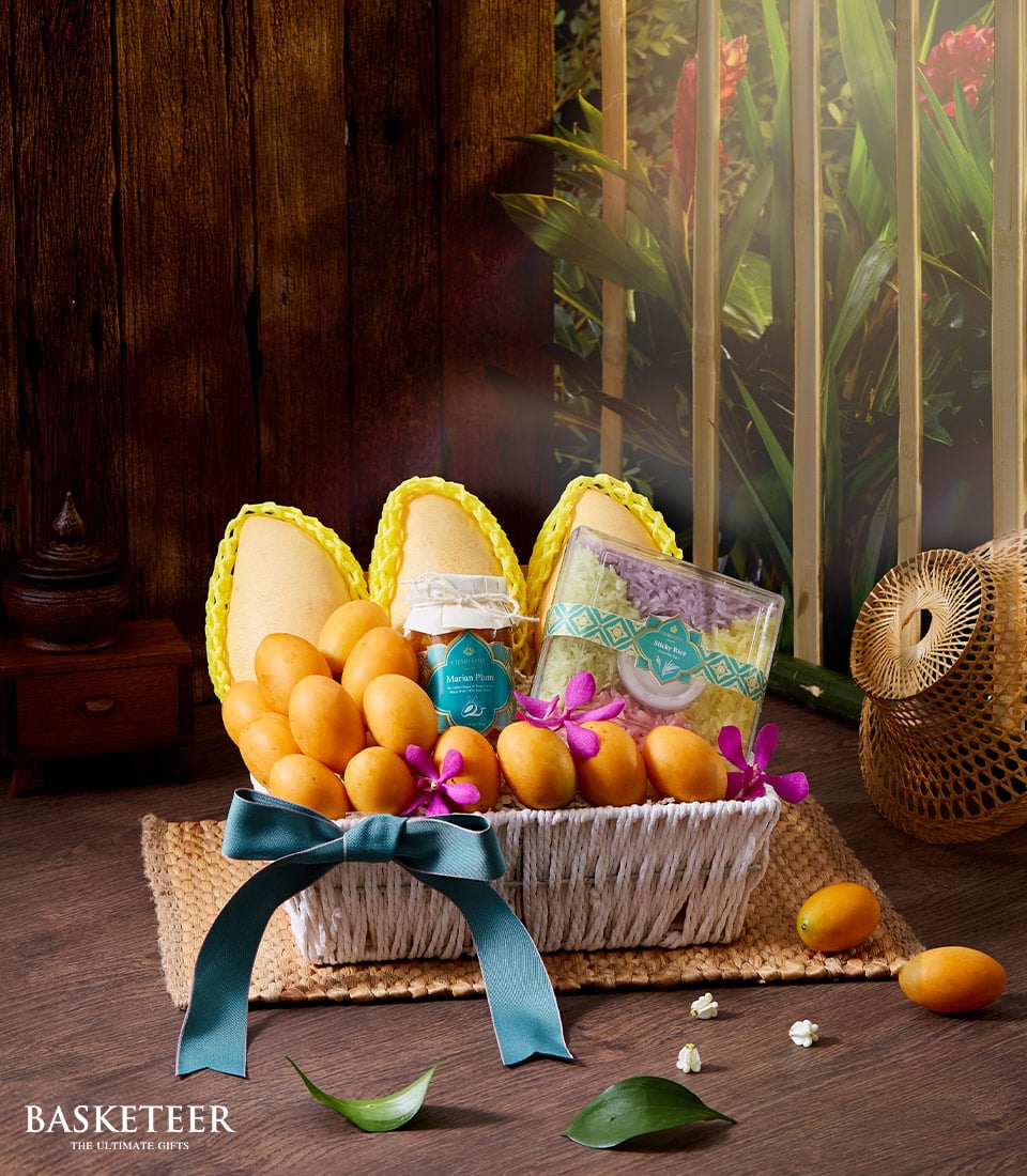 Thai Songkran fruit basket with mango, marian plums, sticky rice, and purple orchids in woven white basket with teal ribbon