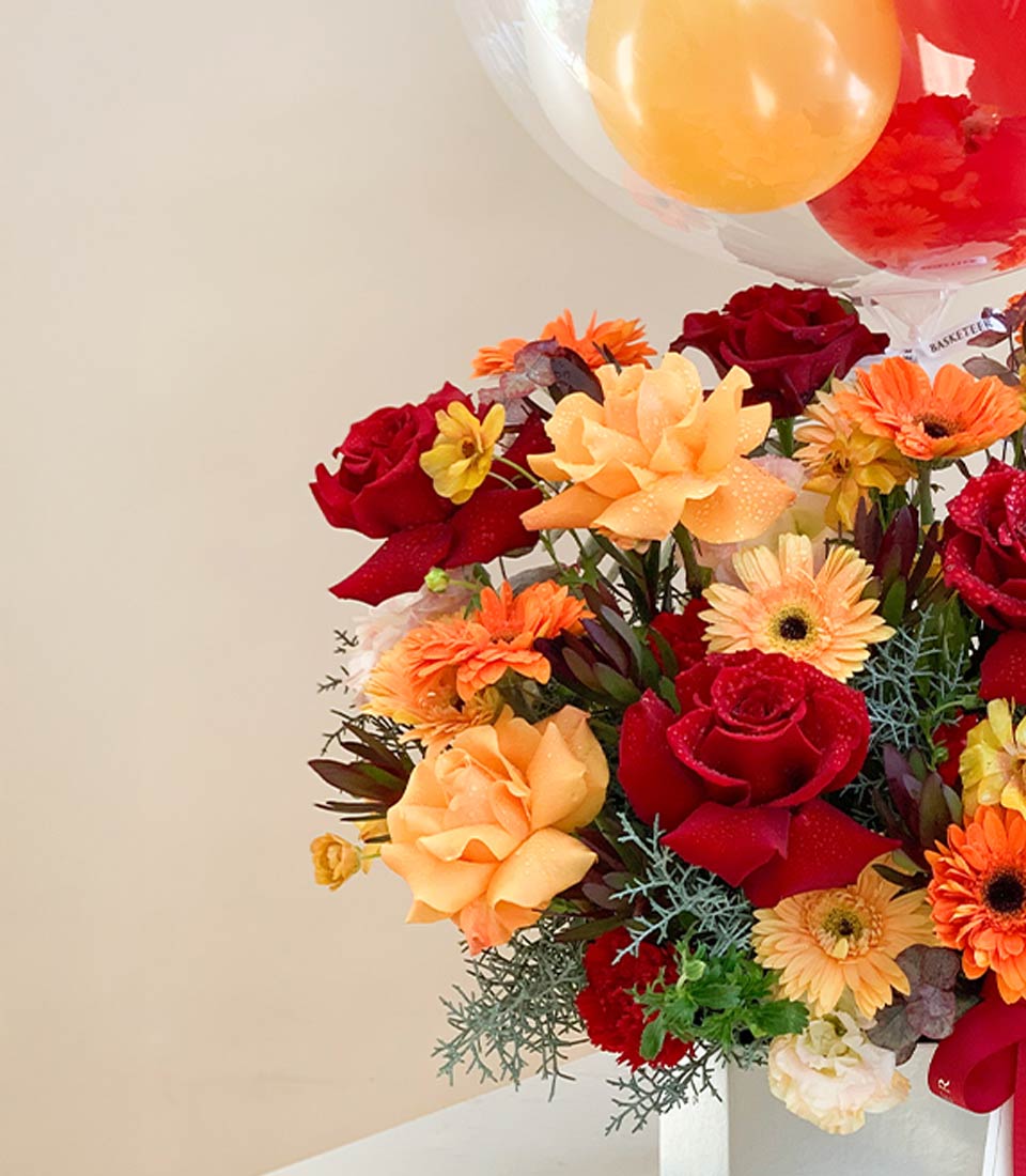 Vibrant red and orange rose bouquet with gerbera daisies and iridescent balloons, artisan birthday flower gift