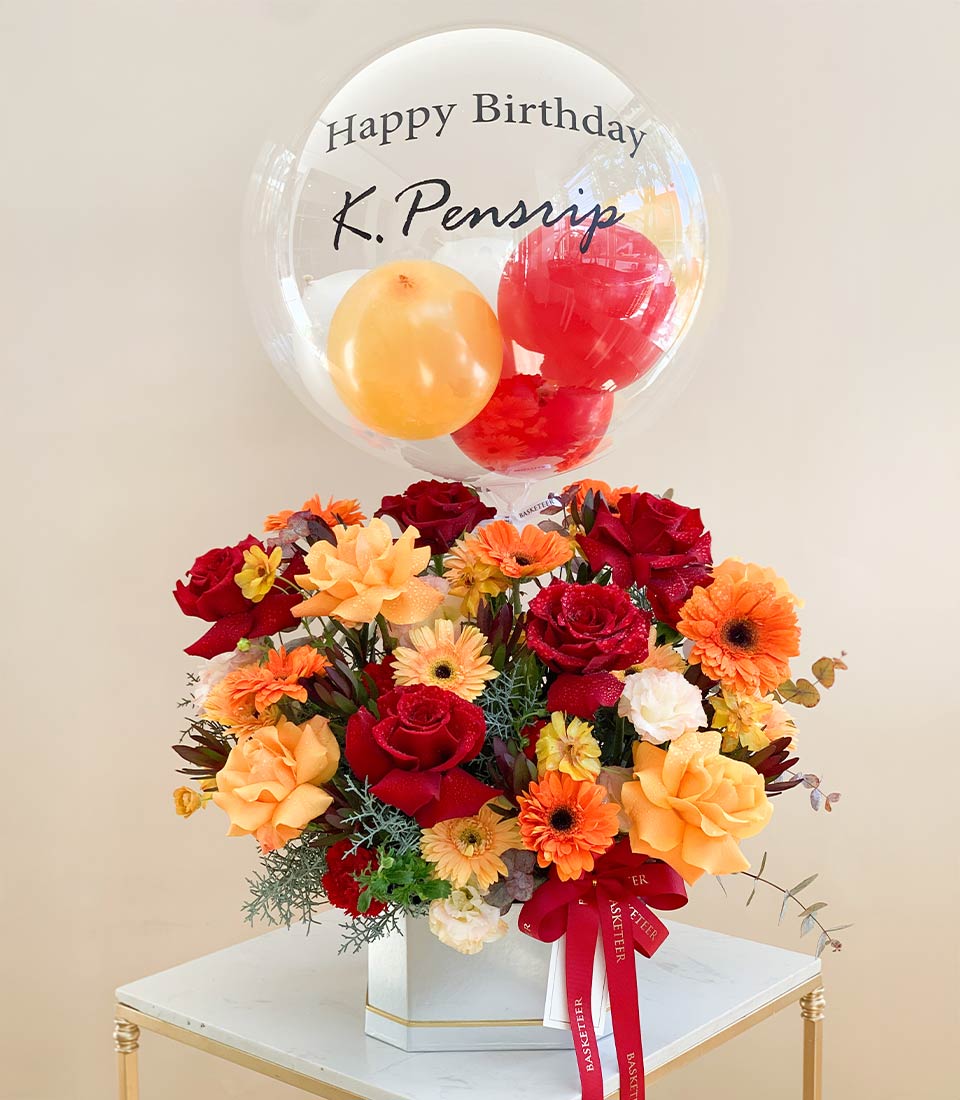 Vibrant red rose and gerbera daisy bouquet in white gift box with gold trim, paired with transparent balloon for birthday