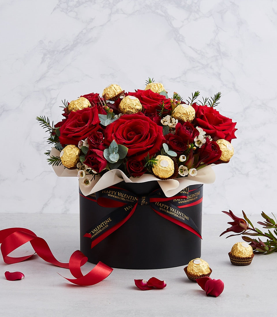 Luxe red roses and Ferrero chocolates in black cylindrical gift box with eucalyptus, perfect for birthdays and anniversaries