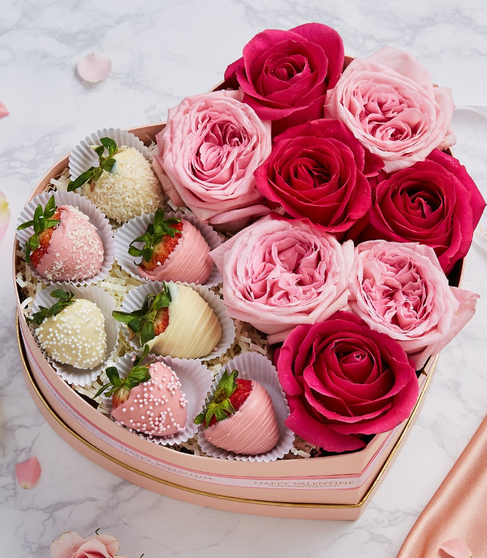 Heart-shaped gift box with chocolate-covered strawberries and fresh roses in pink and fuchsia, anniversary celebration set