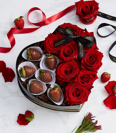 Red roses and chocolate-covered strawberries in black heart-shaped gift box with gold trim