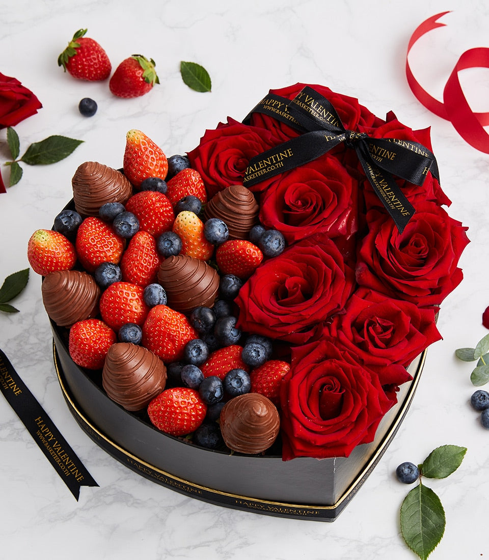 Heart-shaped black gift box with red roses, chocolate strawberries, and fresh berries for anniversaries