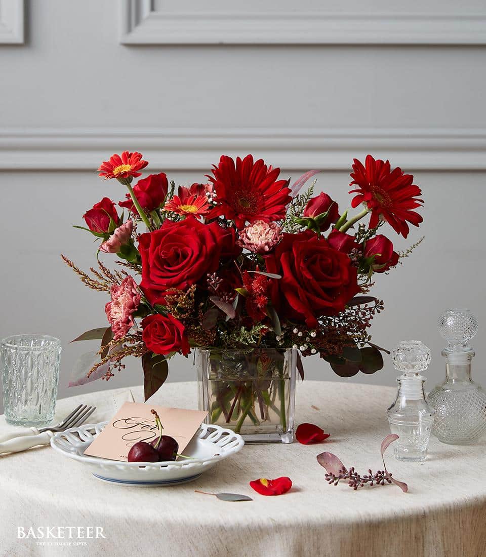 Deep red roses and gerbera daisies in clear glass vase, elegant dining table centerpiece arrangement