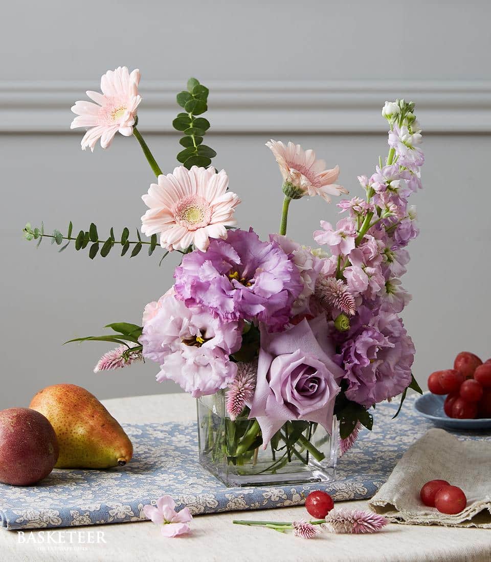 Purple lisianthus and pink gerbera daisies in square glass vase with eucalyptus, fresh flowers for dining table