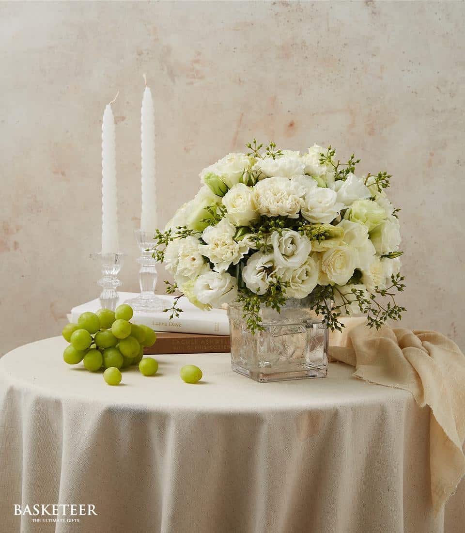 White roses and carnations in clear glass vase with green foliage, elegant dining table arrangement