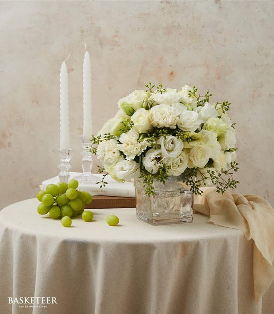 White roses and carnations in clear glass vase with green foliage, elegant dining table arrangement