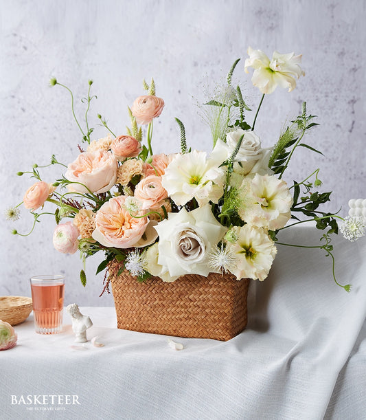 Peach and cream ranunculus with white David Austin roses in a woven basket arrangement for get well wishes