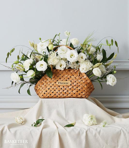 White roses and ranunculus in woven wicker basket with green foliage, get well flowers