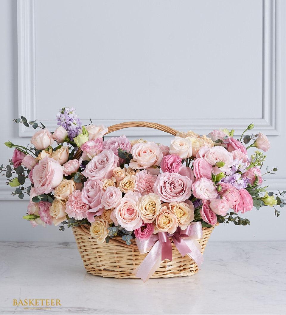 Large wicker basket overflowing with pink and peach roses, carnations, and fresh blooms with satin ribbon bow