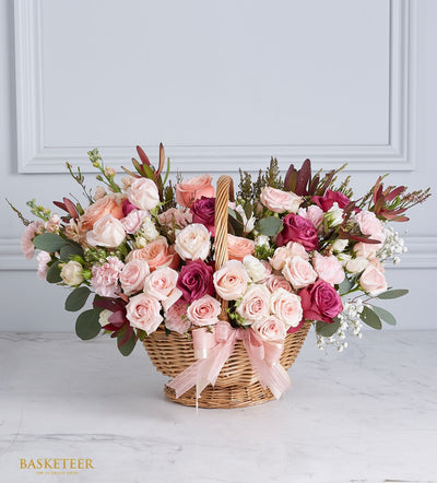 Oval wicker basket with vibrant fresh roses in pink, peach, cream and magenta, white baby's breath, light pink satin ribbon