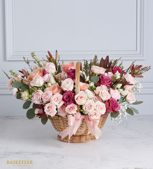Oval wicker basket with vibrant fresh roses in pink, peach, cream and magenta, white baby's breath, light pink satin ribbon