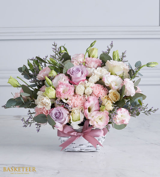Soft pastel roses and lisianthus in white woven basket with dusty rose satin bow