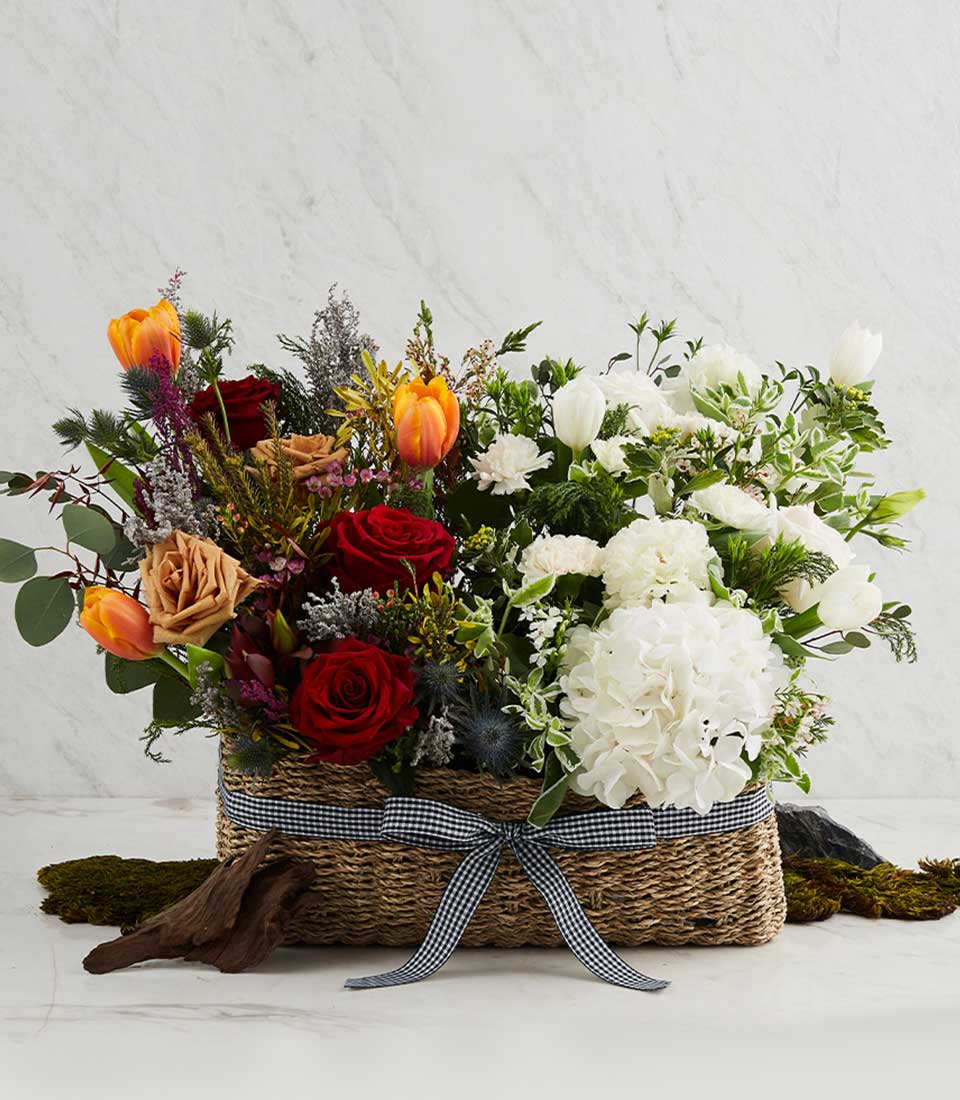 Rustic woven basket with vibrant mixed flowers, red roses and white hydrangea arrangement with gingham ribbon