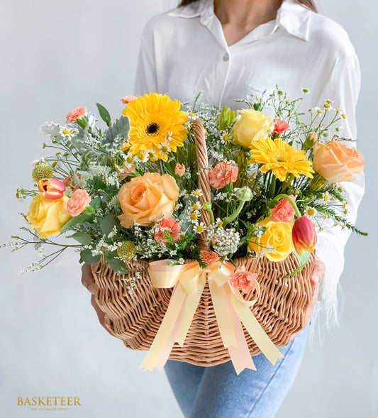 Fresh flower arrangement in wicker basket with yellow gerberas, peach roses, and tulips for get well wishes