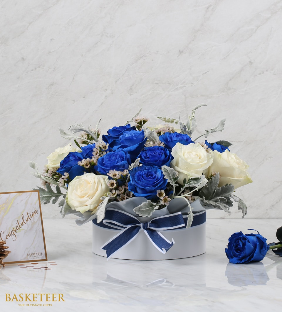 Royal blue and cream roses in white hatbox with striped ribbon bow, congratulations gift arrangement