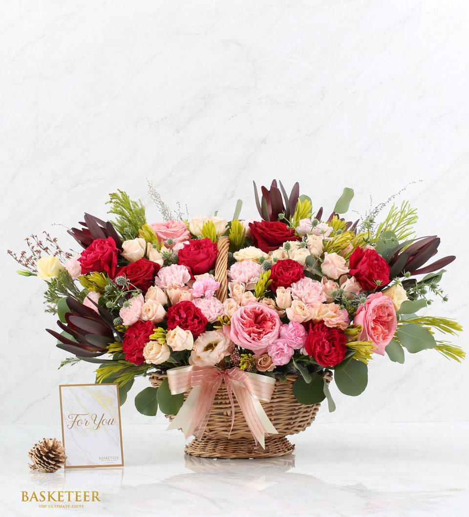 Grand Romance luxury flower basket with red roses, pink carnations, and cream blooms in woven wicker