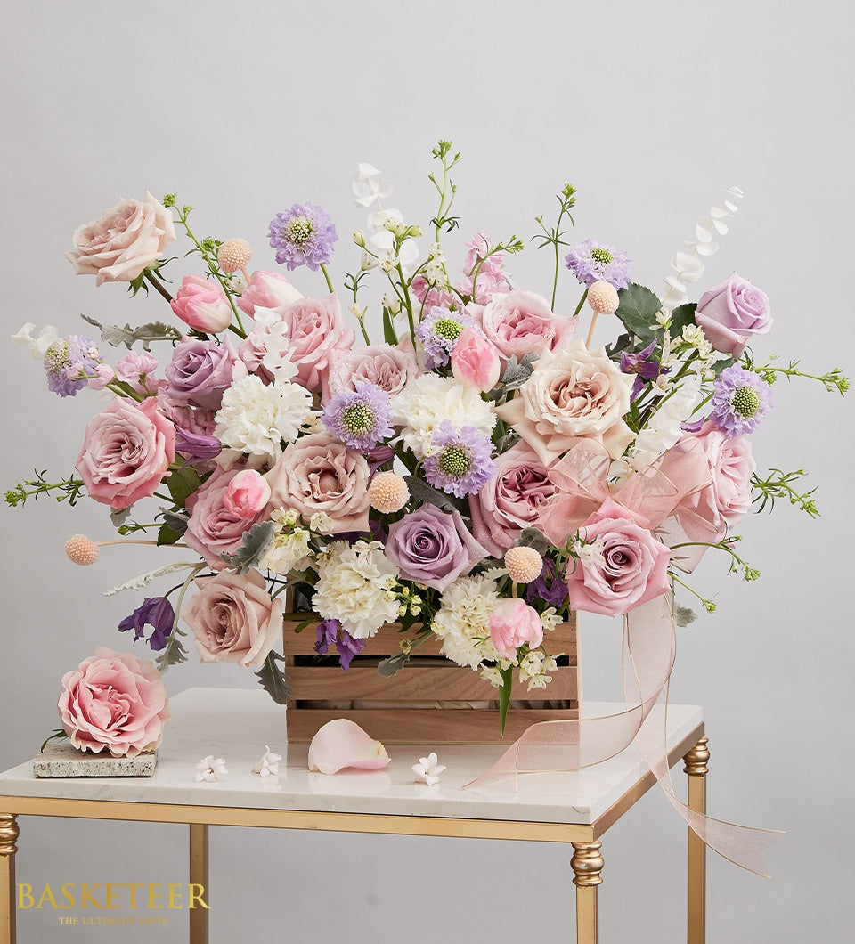 Pastel pink and lavender roses, tulips, and scabiosa in wooden crate with pink ribbon, get well flowers