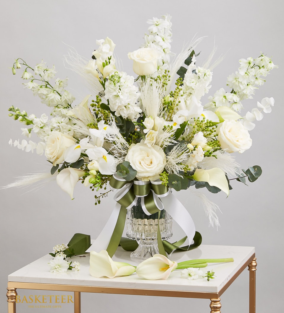 Elegant white flower arrangement with roses, calla lilies, and pampas grass in clear glass vase