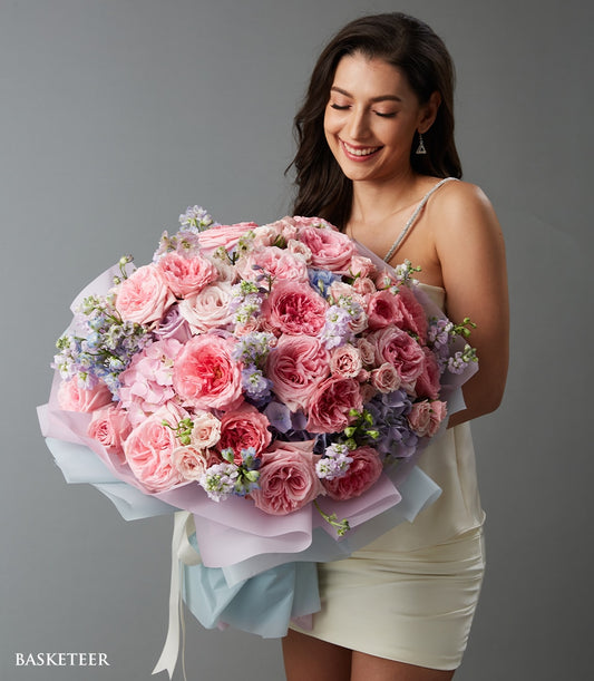 Woman holding luxury pink rose and hydrangea bouquet with lavender filler, wrapped in pastel tissue and white ribbon