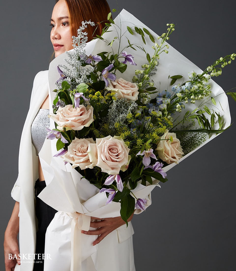 Elegant Valentine's bouquet of light pink roses, purple clematis, and blue flowers with cream ribbon wrap