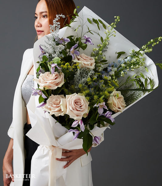 Elegant Valentine's bouquet of light pink roses, purple clematis, and blue flowers with cream ribbon wrap