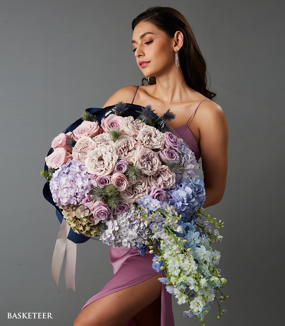Luxury cascading bouquet of pink garden roses, blue thistle, purple hydrangeas, and trailing delphiniums wrapped in dark