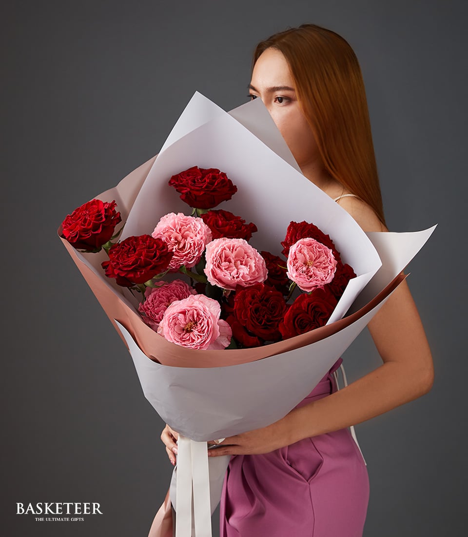 Woman holding lush bouquet of deep red and blush pink roses wrapped in kraft paper, Valentine's Day gift