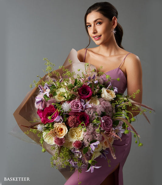 Luxe mixed rose bouquet in red, pink, and cream with purple accents, held by woman in lavender slip dress
