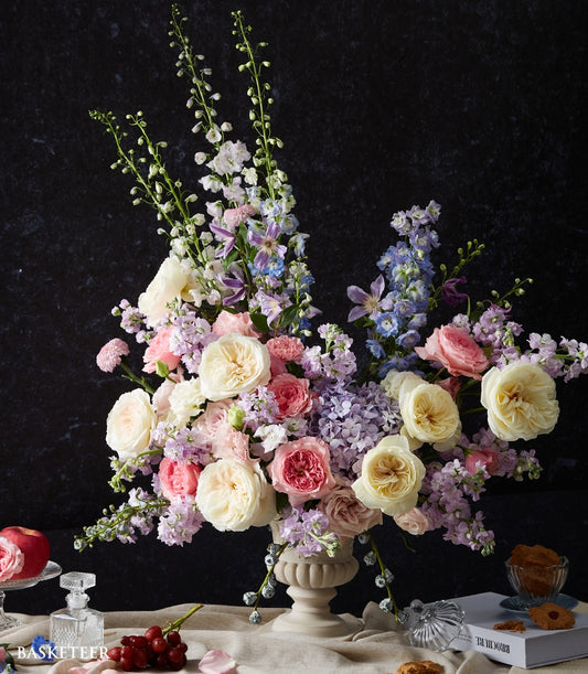 Pastel Symphony floral arrangement in cream urn vase with pink roses, delphiniums, and hydrangeas