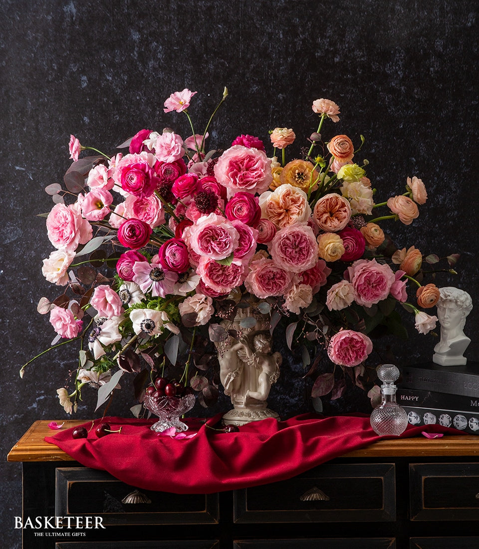 Luxe pink and peach rose arrangement with ranunculus and anemones in cream cherub vase