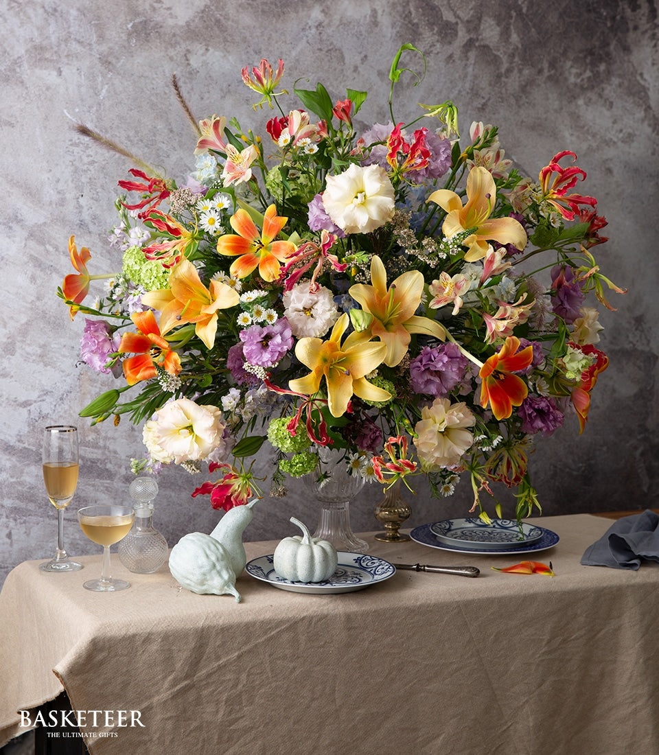 Vibrant mixed flower arrangement with orange lilies, pink and purple blooms in clear glass vase for celebrations