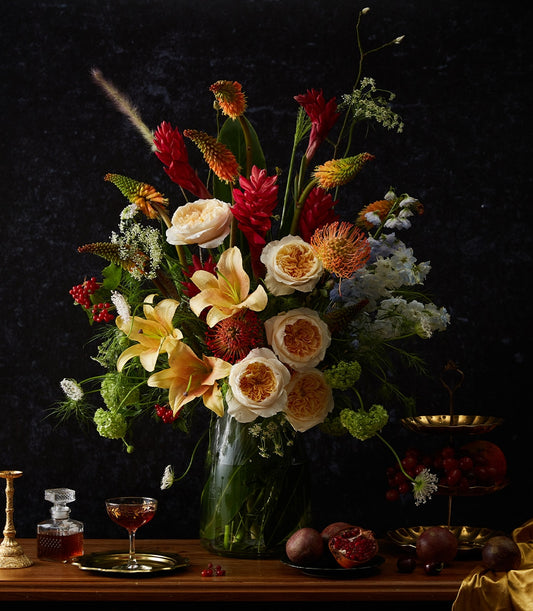 Lavish mixed-flower arrangement with garden roses, protea, and lilies in clear glass vase, luxury gift styling
