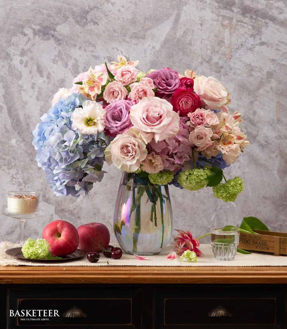 Vibrant blue hydrangea and rose bouquet with pink lisianthus in clear glass vase, fresh flowers for celebrations and gifting