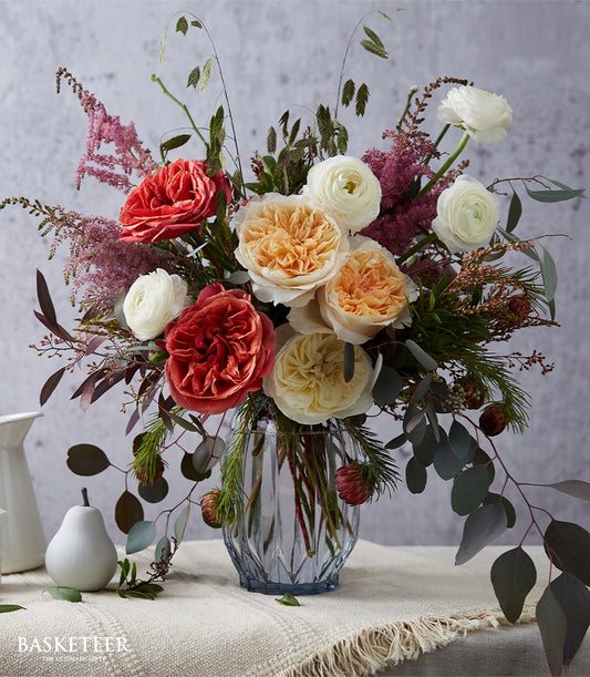 Timeless English-style floral arrangement with red roses, ranunculus, and astilbe in clear faceted vase by Flowers by