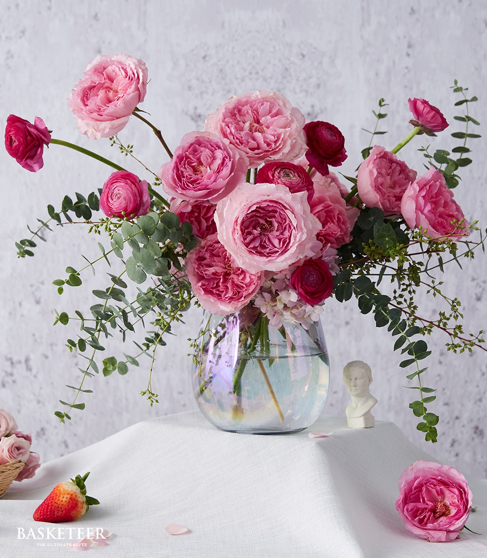 Dark pink roses and ranunculus in iridescent glass vase with eucalyptus greenery